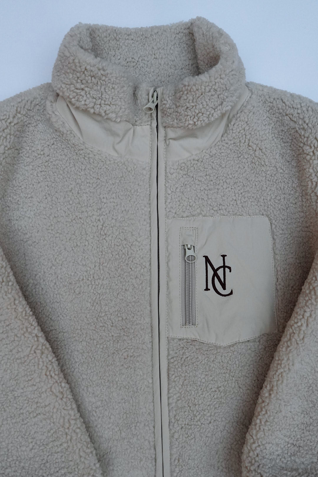 Cosy Teddy Jacket: Cream sherpa-fleece jacket with full zipper, stand-up collar, and chest pocket embroidered with NC, ideal for keeping warm in winter.