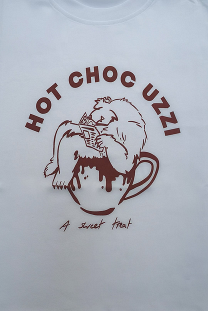 White T-shirt with cartoon animal lounging in a mug, labeled HOT CHOC UZZI and A sweet treat, perfect for winter coziness.