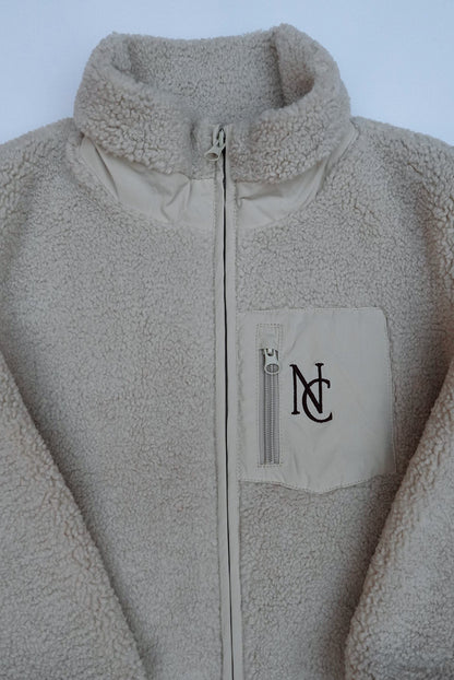 Cosy Teddy Jacket: Cream sherpa-fleece jacket with full zipper, stand-up collar, and chest pocket embroidered with NC, ideal for keeping warm in winter.
