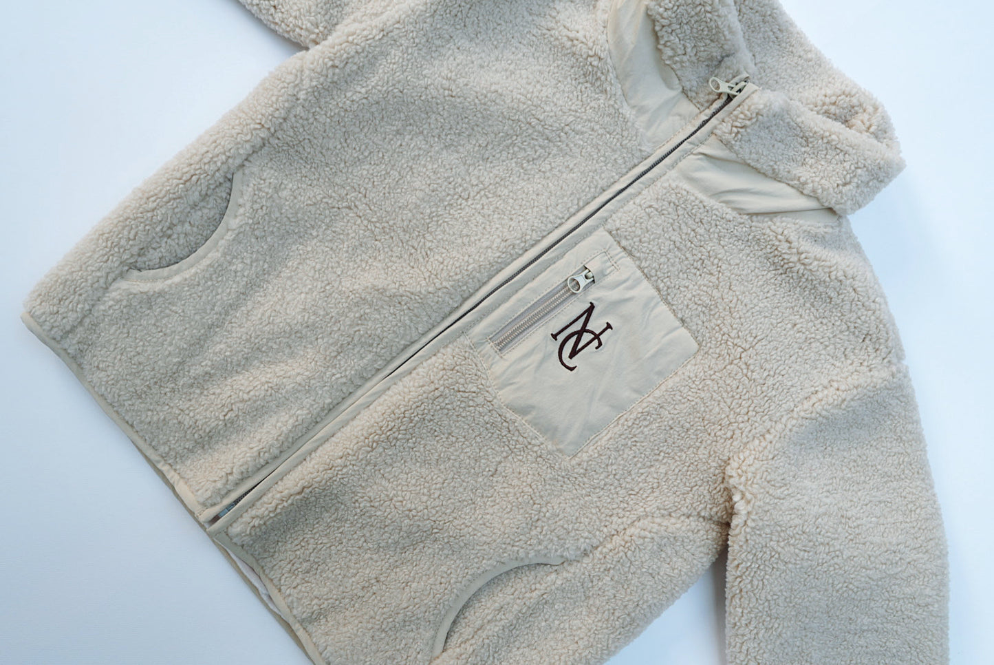 Cosy Teddy Jacket with full-length zipper, hand-warmer pockets, a chest zip-pocket featuring an NC logo; designed for warmth and style in cold seasons.