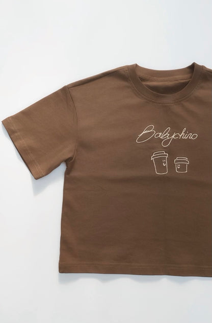 Babychino Tee featuring a white cursive graphic with smiling coffee cups, crafted from premium cotton for a comfortable, oversized fit perfect for kids' everyday wear.